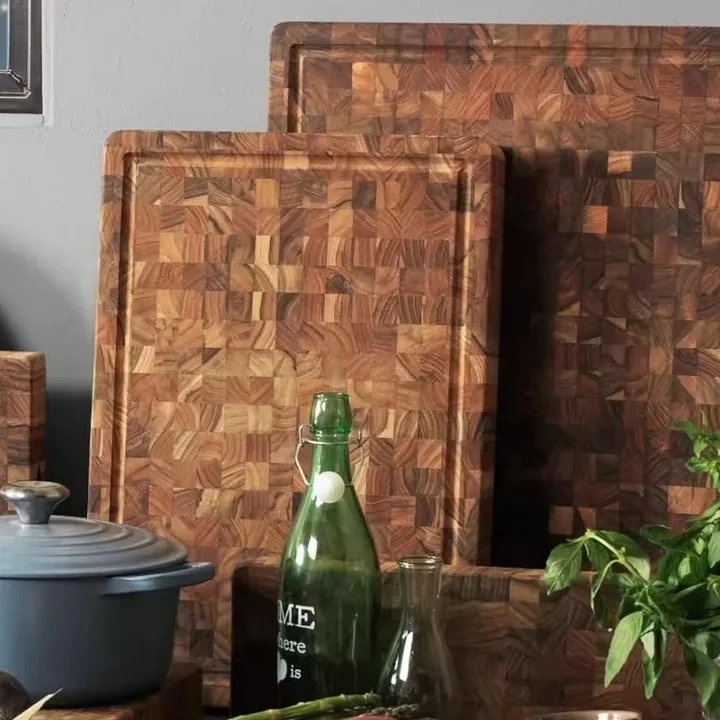 Teak end-grain cutting boards leaning against a wall behind a green glass bottle