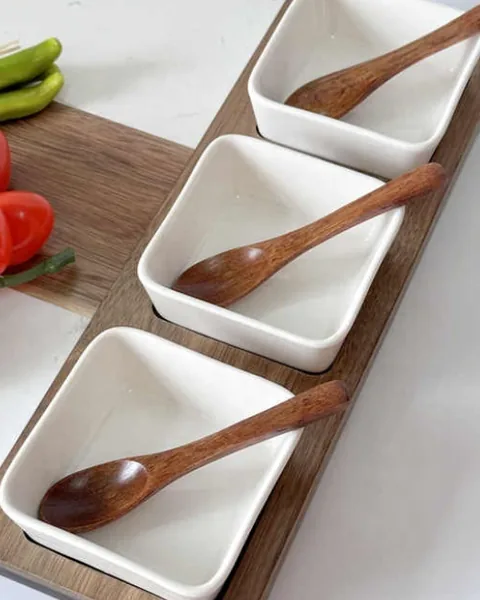 Three white porcelain dishes with wooden spoons on a walnut serving board